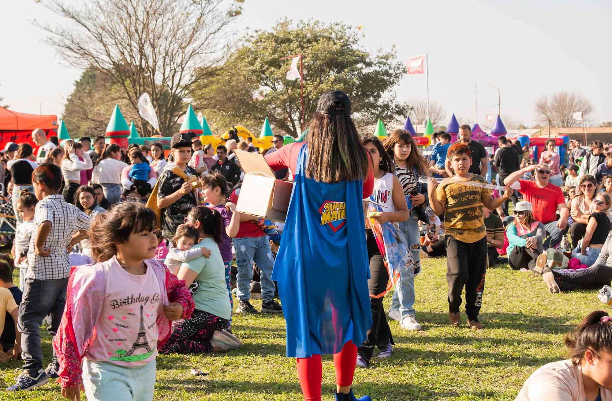 Persona con capa de SuperMaira caminando entre la multitud en un evento comunitario